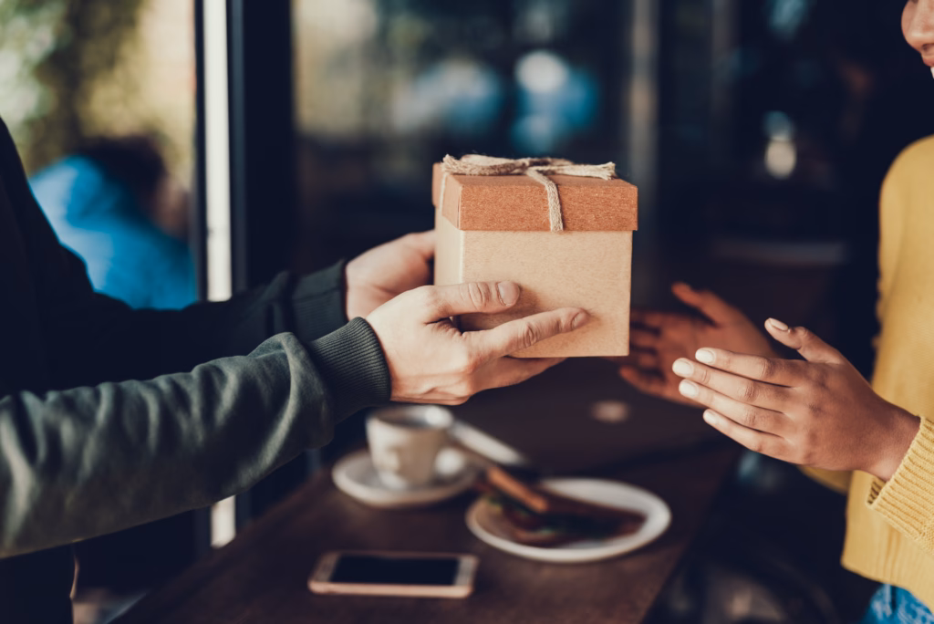 Sweet moments concept. Cropped photo hands with gift. Man sharing present to her woman. They standing inside cafe