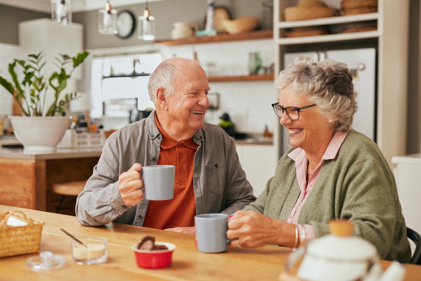 An older couple with mugs of tea at their kitchen table